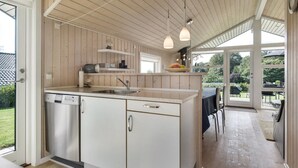 A modern kitchen with wooden paneling, a central island, and a view to an outdoor patio. - "Rathi" - 250m from the sea by Interhome (Haarby)