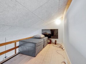 Cozy attic retreat with a single bed, flat-screen TV, and wooden railing.