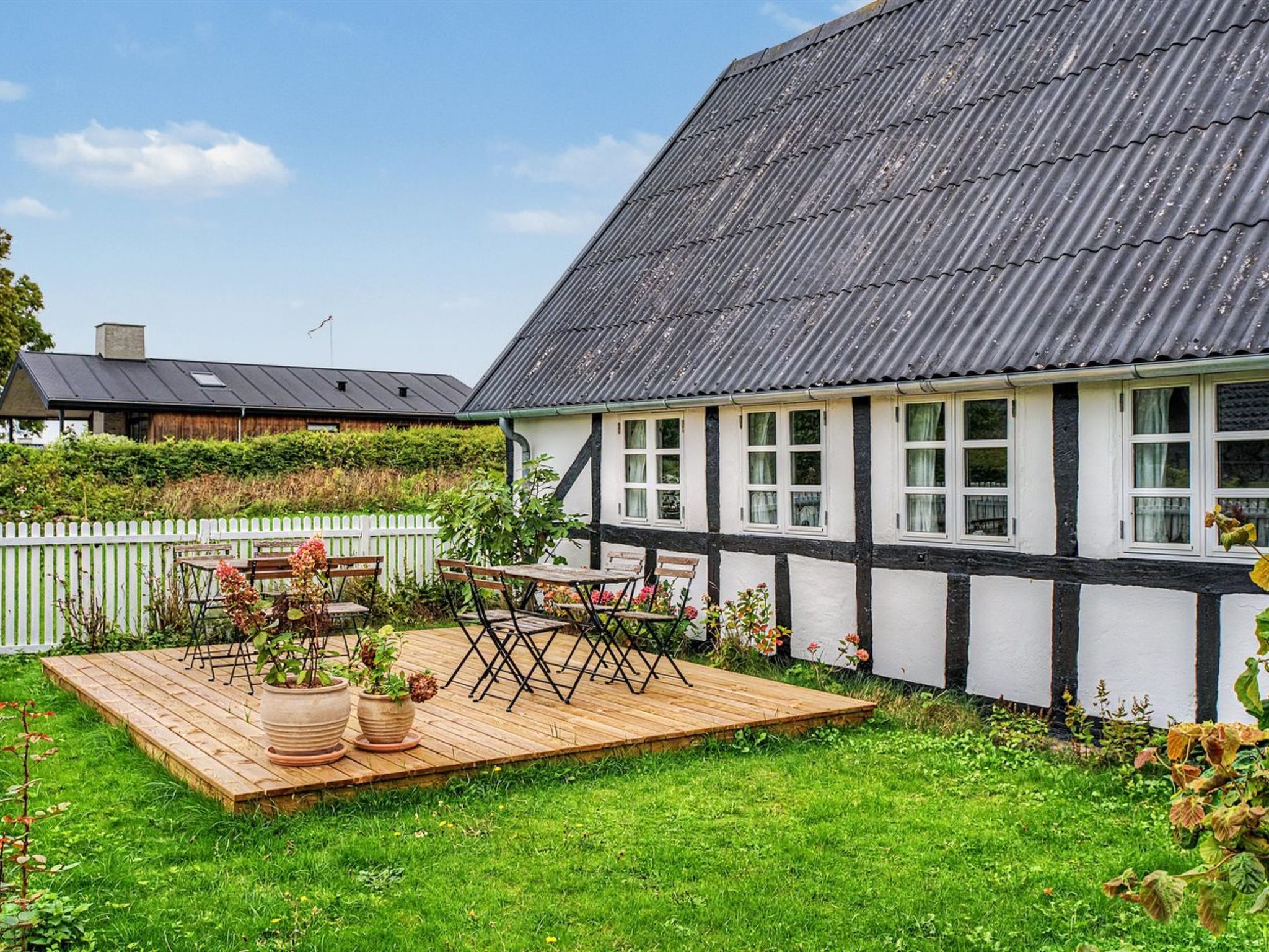 A house with a sloped roof, a wooden deck, and a garden with potted plants.