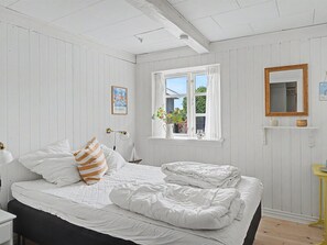 Une chambre à coucher avec un lit, une fenêtre avec des rideaux, une table de chevet et un miroir au mur.