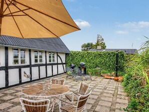Une cour avec une table ronde et des chaises, un grand parasol et un bâtiment à la façade noire et blanche.