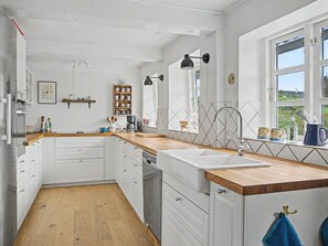 Une cuisine avec des meubles blancs, un plan de travail en bois, un évier et une fenêtre donnant sur un beau paysage.