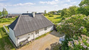 Ein weißes Haus mit geneigtem Dach, einer Schotterauffahrt und einem Garten mit blühenden Blumen.