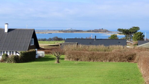 Ein Küstenanwesen mit Rasengrundstück, einem Haus mit dunklem Dach und Blick aufs Meer.