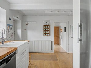 Une cuisine dotée d’un plan de travail en bois, de meubles blancs, d’un lave-vaisselle encastré et d’un radiateur.