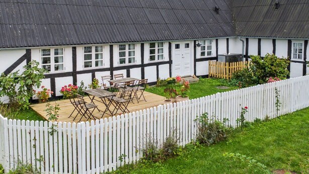 Una casa tradizionale con struttura a graticcio e un giardino recintato con area salotto esterna.