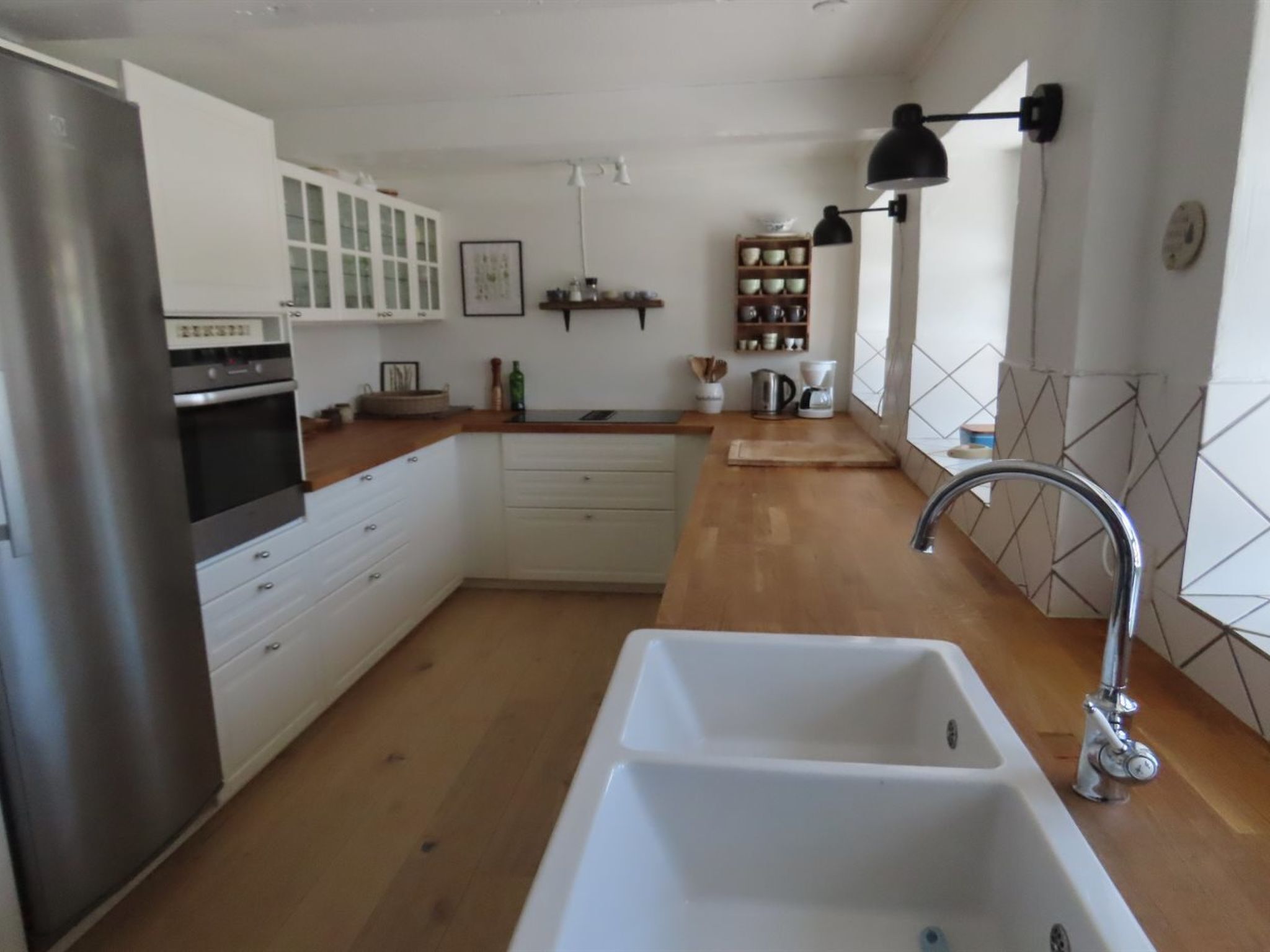 Une cuisine moderne avec des armoires blanches, un réfrigérateur en acier inoxydable, un four encastré, un évier doté d’un robinet contemporain et un plan de travail en bois.