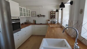 Eine moderne Küche mit weißen Schränken, einem Edelstahl-Kühlschrank, einem eingebauten Backofen, einer Spüle mit modernem Wasserhahn und einer Holz Arbeitsplatte.