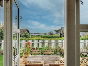 Une porte ouverte donnant sur une terrasse en bois, avec un banc et des plantes en pot.