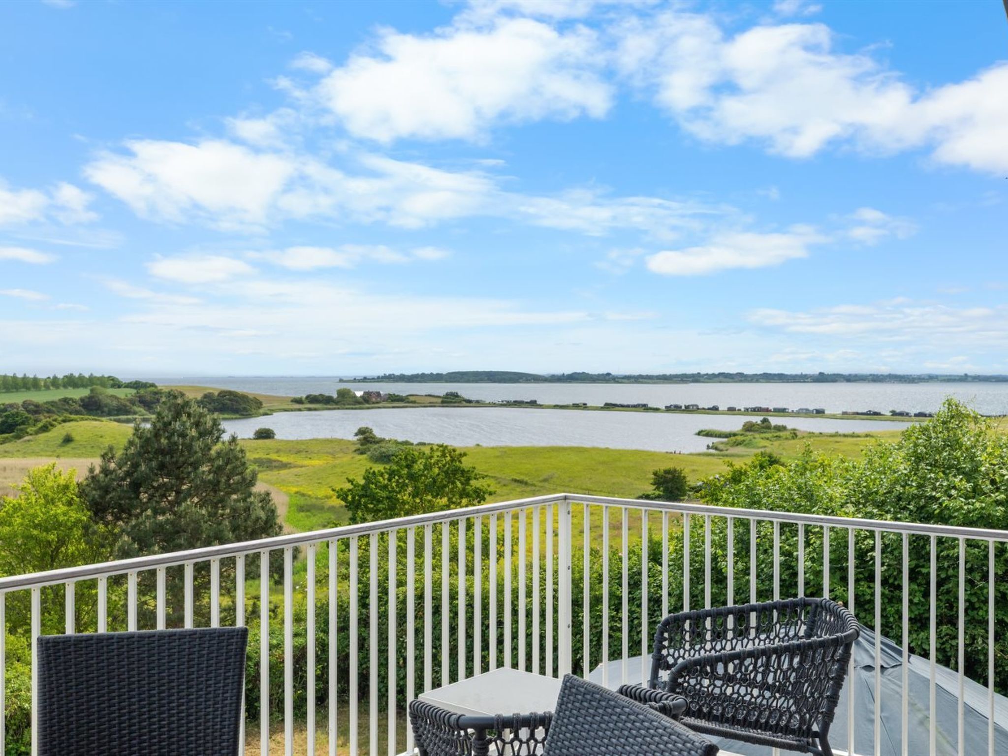 Ein Balkon mit Korbmöbeln, der auf einen See und eine entfernte Landschaft blickt.