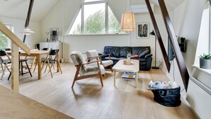 Un loft spacieux avec de hauts plafonds, un coin repas avec des meubles en bois, un canapé en cuir noir et de grandes fenêtres laissant entrer la lumière naturelle.