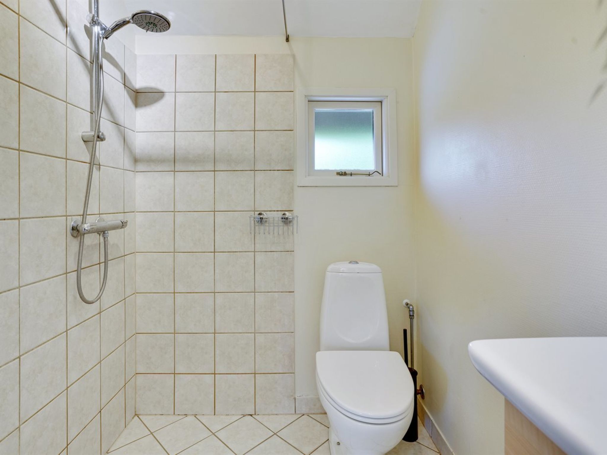 A small bathroom with a shower, toilet, and a window.