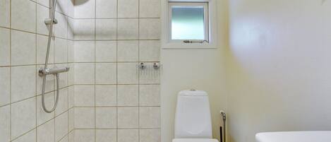 A small bathroom with a shower, toilet, and a window.