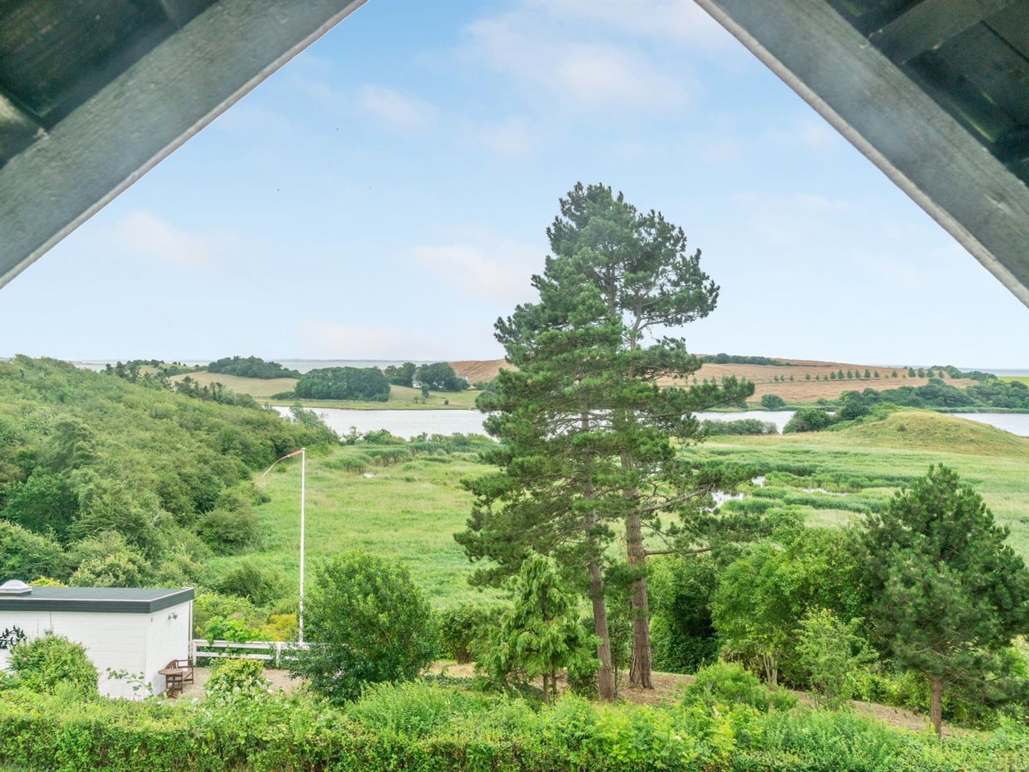 Une vue prise depuis sous un pont, donnant sur un paysage verdoyant avec un lac et une colline au loin.