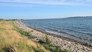 Une plage côtière avec un rivage sablonneux, une jetée qui s’avance dans l’eau et un ciel dégagé.