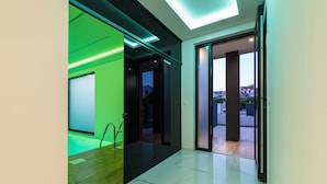 Corredor moderno com porta de vidro que dá para o exterior, chão de madeira e parede iluminada em verde.
