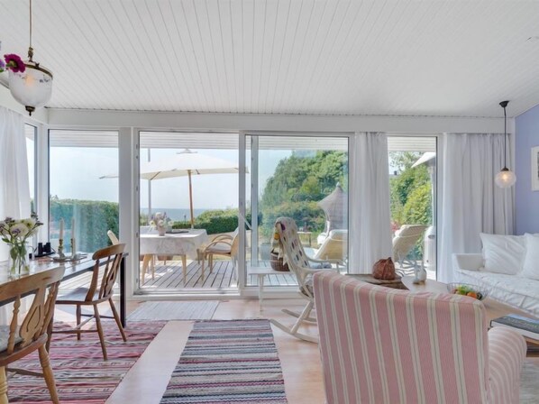 Relax in this serene space with a dining table, sofa, and armchair, leading to an outdoor area.