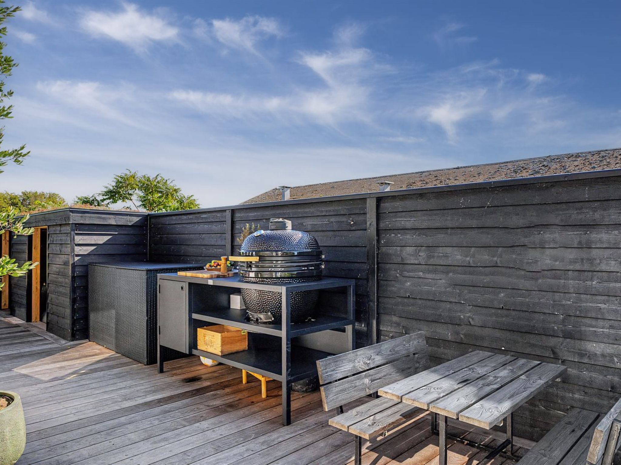 An outdoor patio with a grill, seating, and a wooden deck.