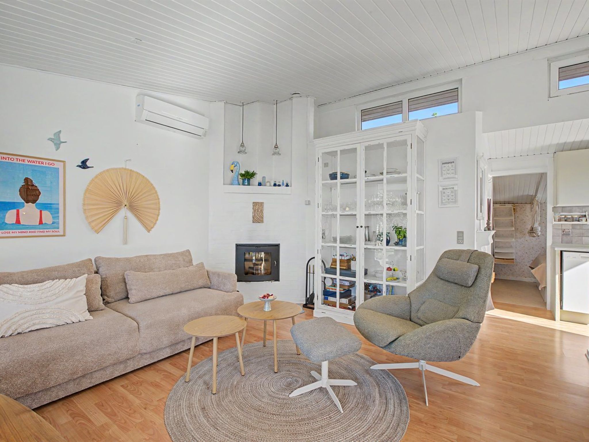 A modern living room with a sofa, armchair, and a small table. There is a bookshelf and a window with blinds.