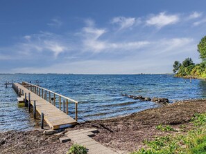 A wooden pier extending into calm waters, a rocky shoreline, and a clear sky.