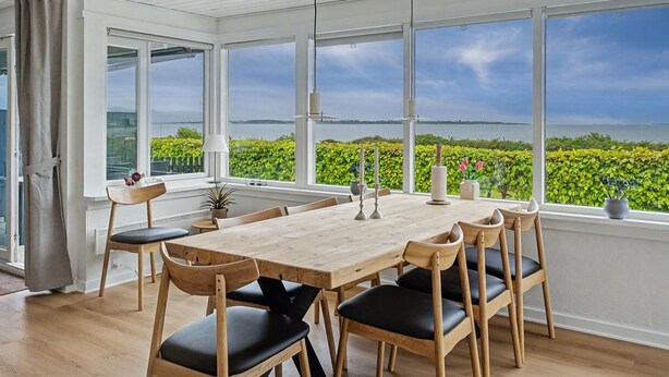 A spacious dining area with a large table and chairs, large windows with a view of greenery and water, and a white ceiling with exposed beams. - "Annalia" - 50m from the sea by Interhome (Faaborg)