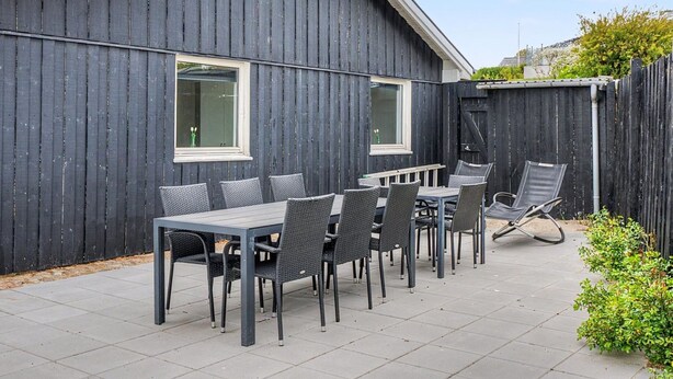 Eine Terrasse mit Tisch und Stühlen, ein Holzzaun und ein Gebäude mit Fenstern.