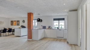 A modern kitchen with white cabinetry, a brick accent wall, and a dining area with a white table and chairs.