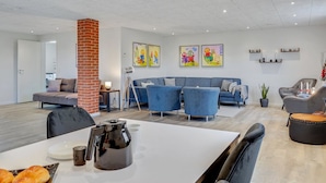 A modern living room with a sofa set, a coffee table, and a dining area with a kettle and croissants.