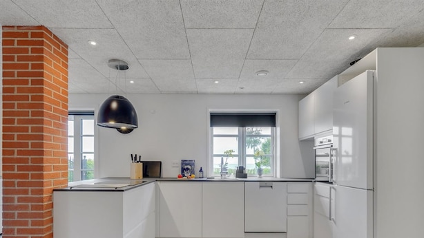 A modern kitchen with white cabinets, a brick column, a black pendant light, and a view of the outdoors.