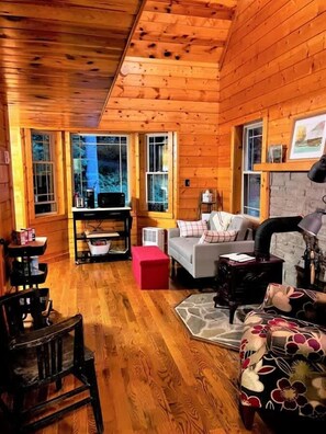 Ein gemütliches Blockhaus-Interieur mit Holzwänden, einer Couch, einem roten Hocker, einem Tisch und einem Kamin.