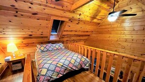 A wooden cabin room with a bed, a nightstand, a lamp, and a ceiling fan.