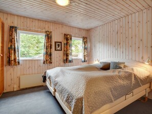 A bedroom with wooden walls, a large bed, and a window with curtains.