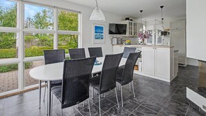 A modern kitchen with white cabinets, a dining area with black wicker chairs, and a large window offering a view of greenery. - "Gullan" - 75m from the sea by Interhome (Middelfart)
