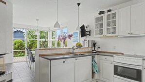 A modern kitchen with white cabinets, a built-in oven, and a large window overlooking a garden. - "Gullan" - 75m from the sea by Interhome (Middelfart)