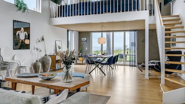 En rummelig opholdsstue med højt til loftet, et spiseområde og en trappe til en overetage.
