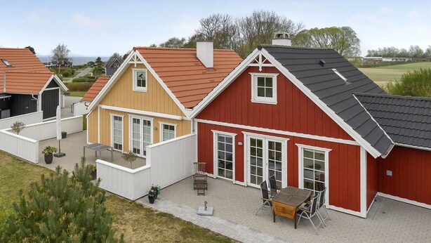En rad hus med röda och gula fasader, vita detaljer och en uteplats med utemöbler.