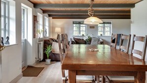 Un comedor amplio con una mesa y sillas de madera, una lámpara colgante y ventanas grandes que dejan entrar luz natural.