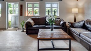 Un salón amplio con techo de madera, un sofá de cuero marrón, una mesa de centro y ventanas grandes con vistas al verdor.