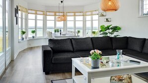 A modern living room with a black sectional sofa, a white coffee table, and large windows offering a view of the sea. - "Hwitserk" - 5m from the sea by Interhome (Otterup)