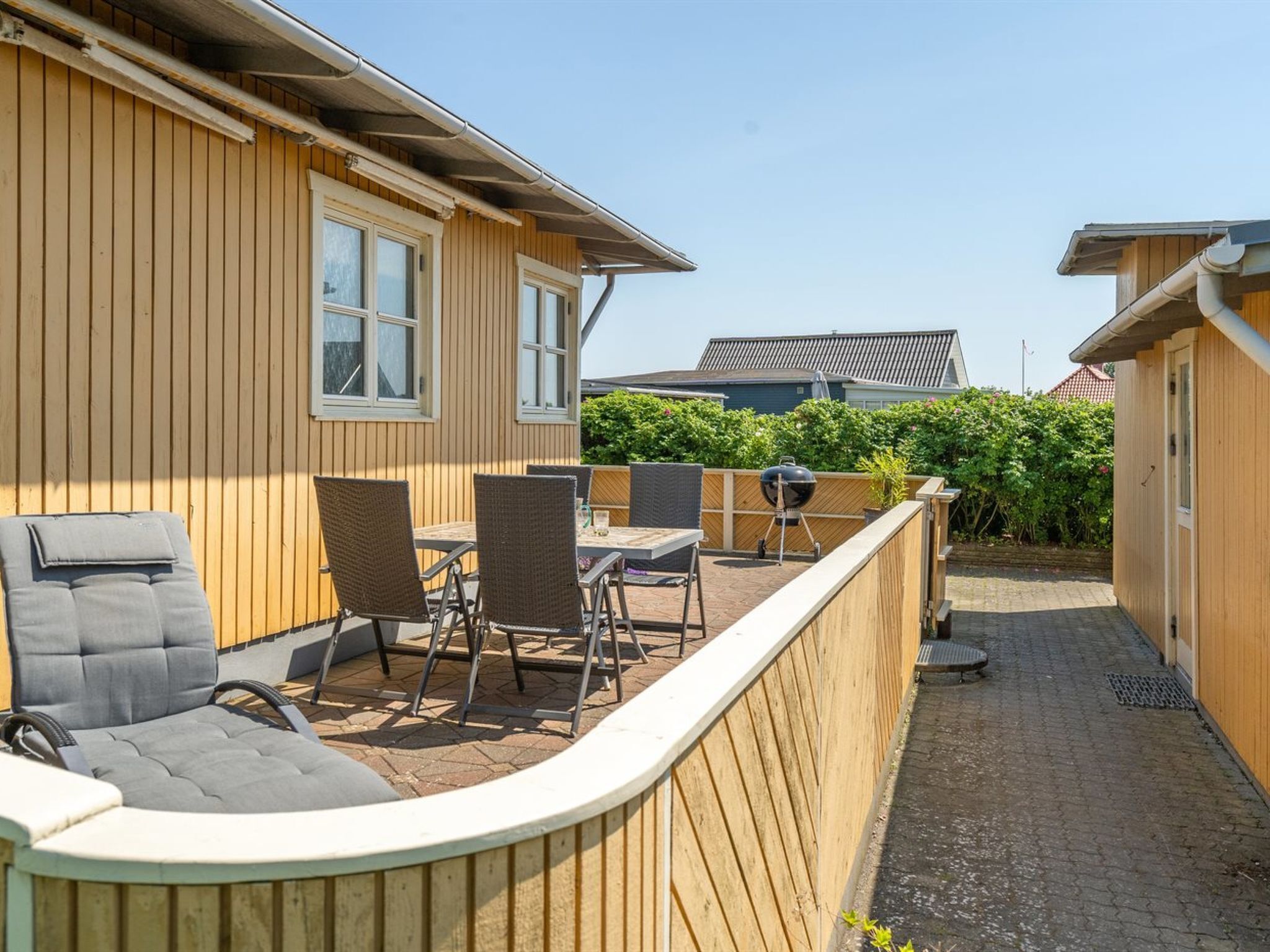 Une maison en bois dotée d’un patio comprenant une table, des chaises et un barbecue.