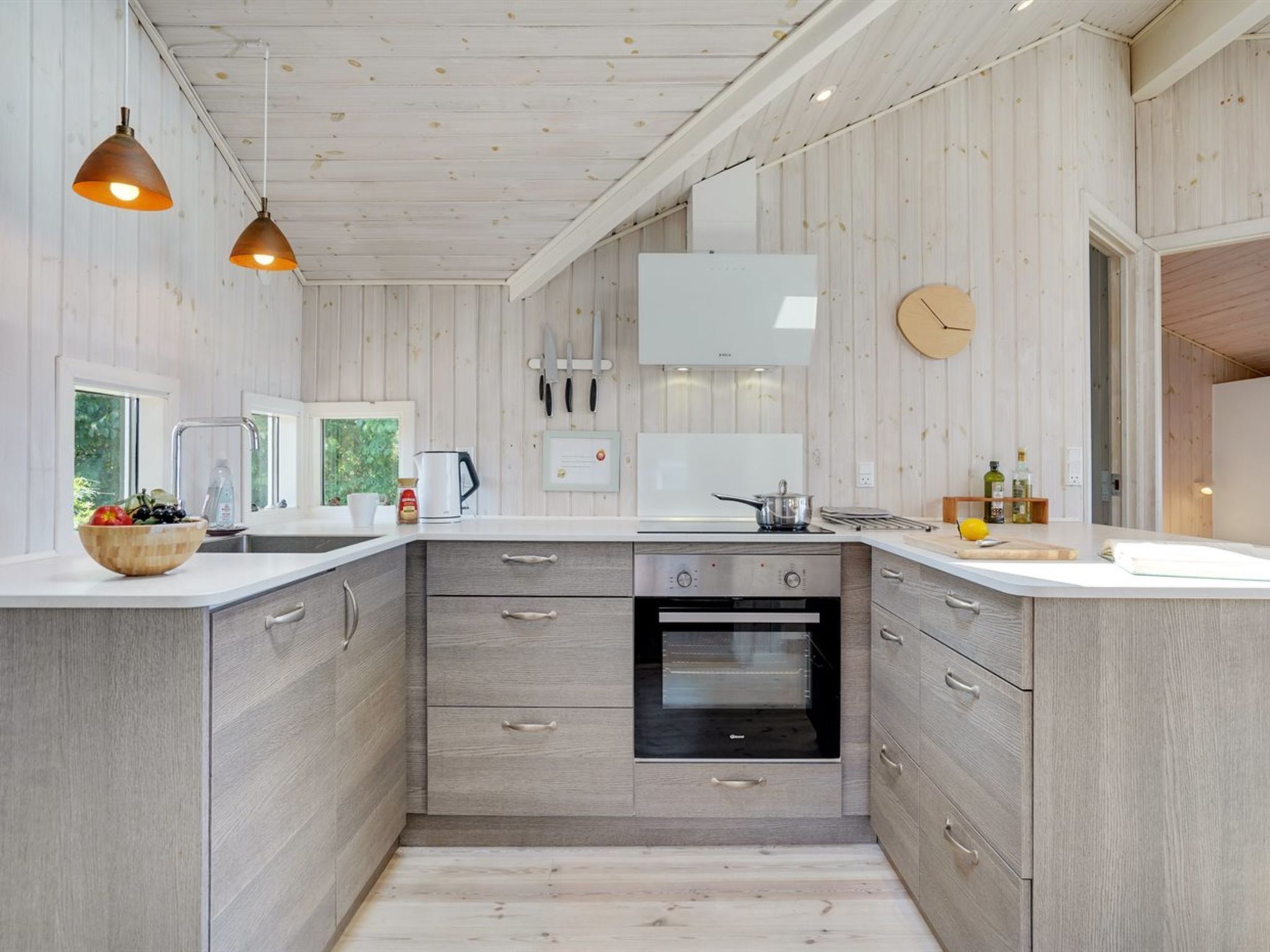 A modern kitchen with wooden paneling, a built-in oven, and a large window.