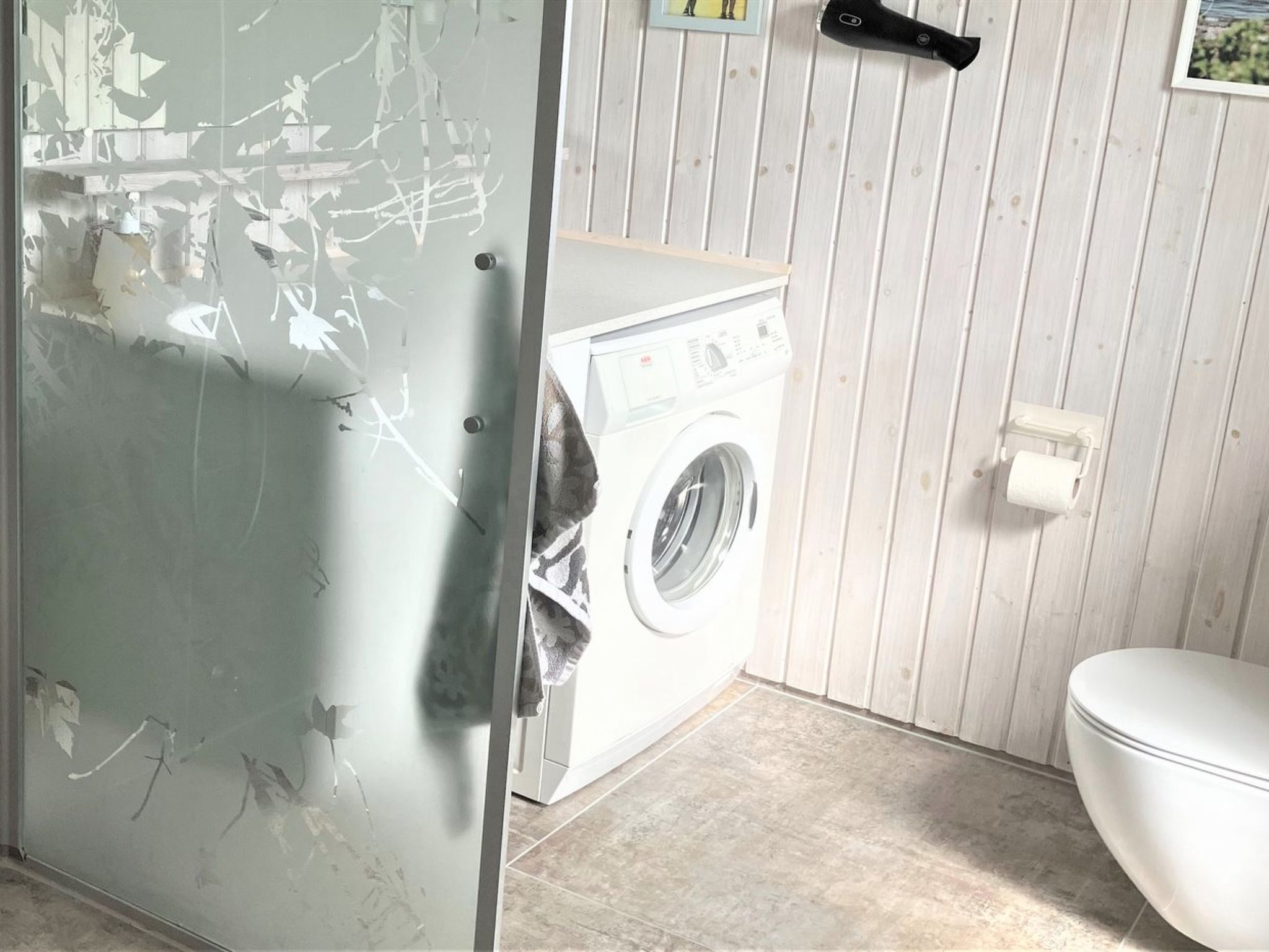 A small laundry room with a washing machine, a toilet, and a towel rack.