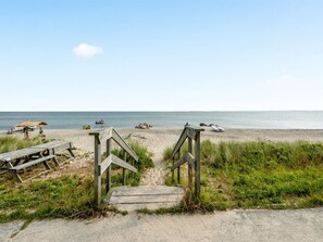 A wooden staircase leading to a sandy beach with a clear view of the ocean.