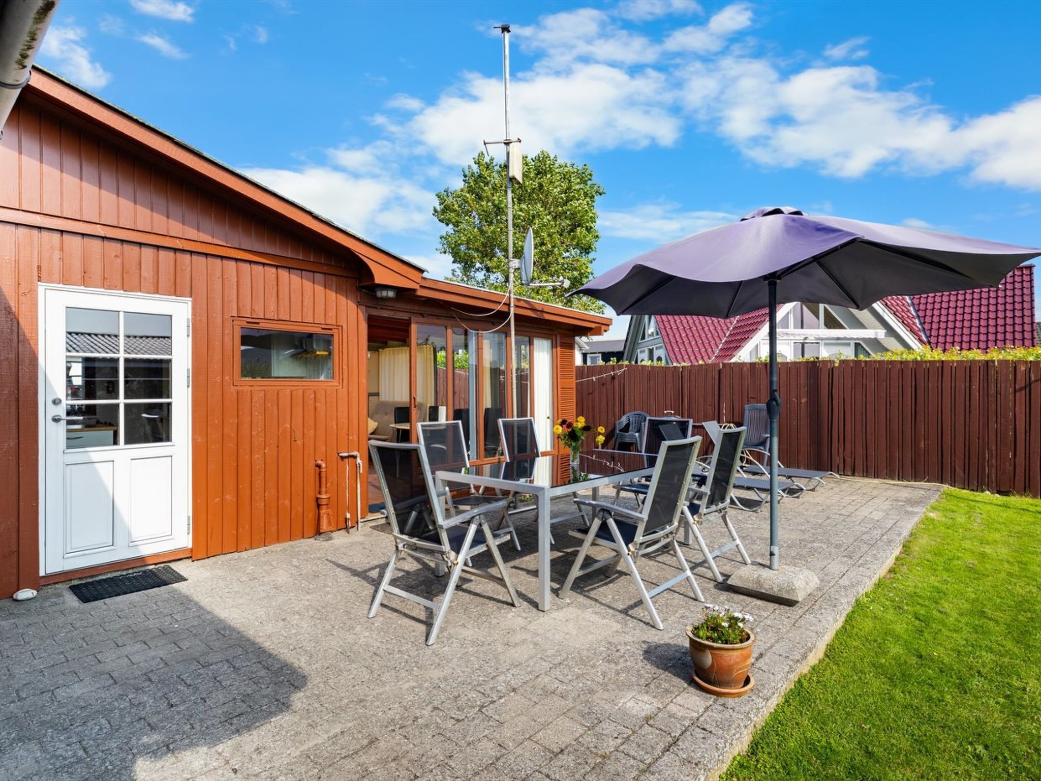 A wooden building with a patio area featuring a table and chairs, a potted plant, and a large umbrella.