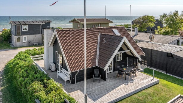 Ein Küstenhaus mit schrägem Dach, einer Terrasse mit Gartenmöbeln und einer Fahnenstange mit einer Flagge.