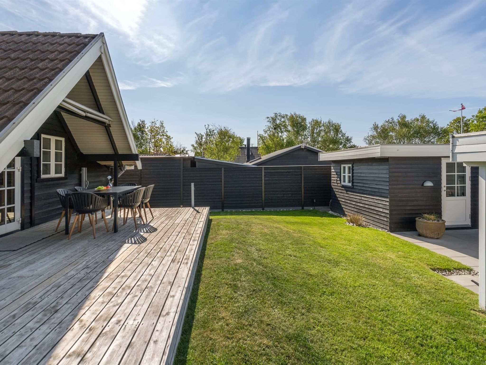 Una casa moderna con una terrazza in legno, un cortile recintato e un piccolo giardino.