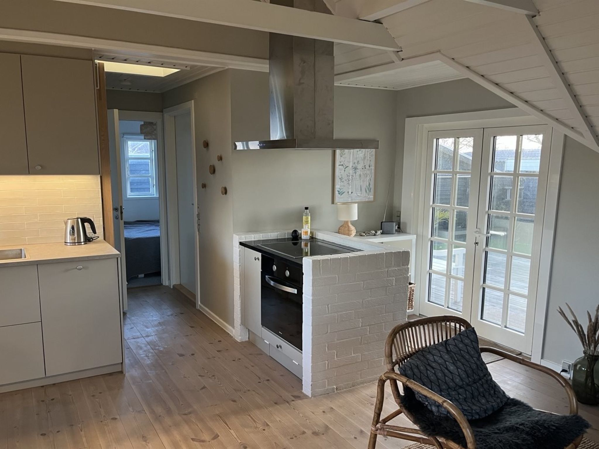 A compact kitchen with a central island, a dining area with a wicker chair, and a large window providing a view.