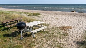 Ein Strand mit einem hölzernen Picknicktisch und einem Grill.