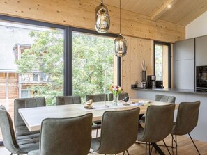 Enjoy meals in this dining area with a large table and six comfortable chairs, surrounded by a wooden ceiling and large windows offering a view of the lush surroundings.