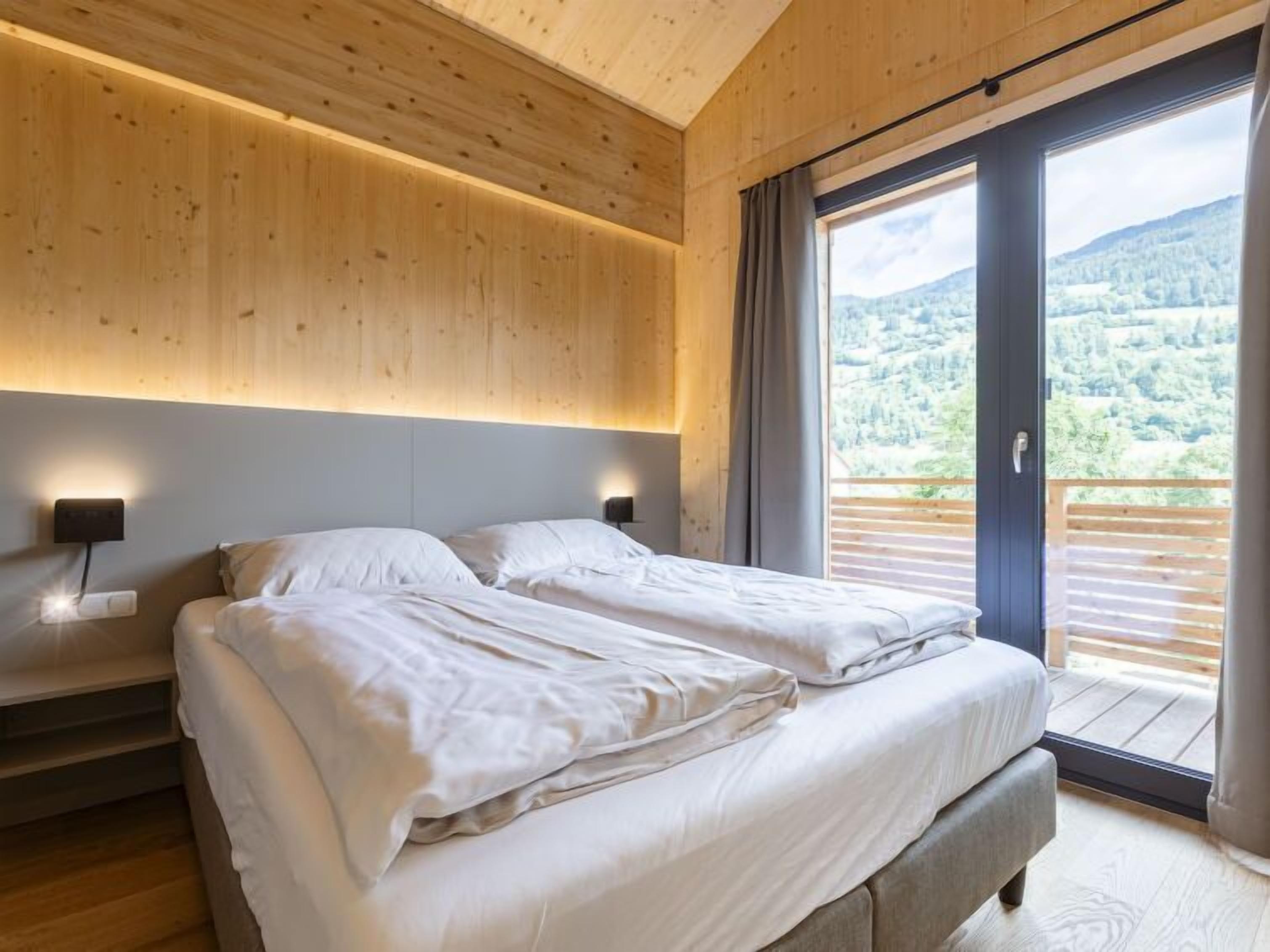 Un dormitorio con dos camas, techo de madera y un ventanal con vistas a una montaña boscosa.